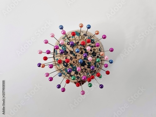 Photos top view of a floral patterned pincushion with multiple colorful pins on it, iso