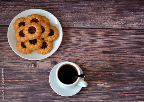 A cup of black coffee and a plate with a pile of kurabye shortbread cookies on a wooden table.