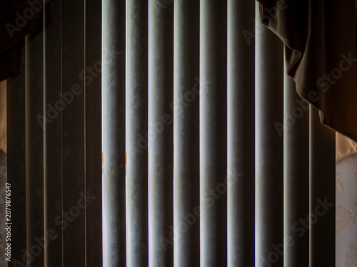 Schilderij op canvas Slices of bright daylight peeking through closed vertical window blinds inside a