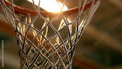Golden sunbeams filter through a woven basketball net, illuminating the hoop