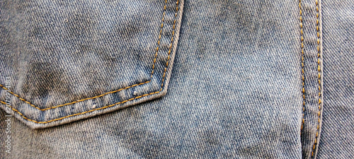 Close-up photo of the texture of a blue denim jeans pocket with double stitching.