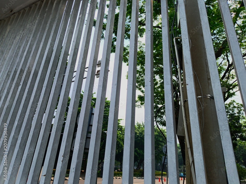 Obraz premium Looking up through white vertical concrete fence bars with green trees backdrop