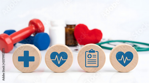 Four wooden blocks with medical symbols on white table with stethoscope and dumbbells