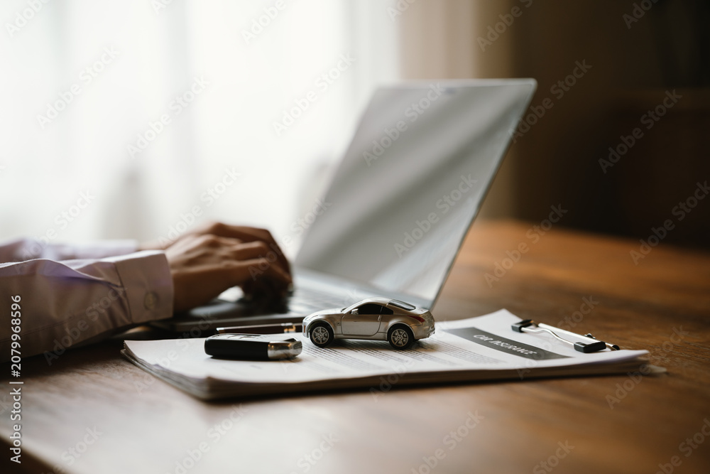 Fototapeta premium Person holding a model car beside a laptop, symbolizing vehicle insurance, auto finance, online car valuation, and ownership.
