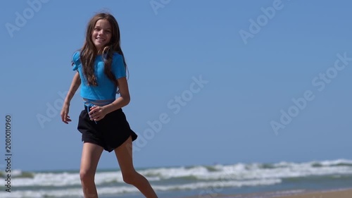A teenage girl strolls along a beach with waves. A girl walks along the seashore or ocean on a sunny day.