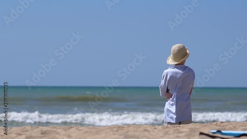 A teenager wearing a hat stands on a tropical island beach, admiring the sunset. A peaceful summer getaway or vacation; summer travel concept.