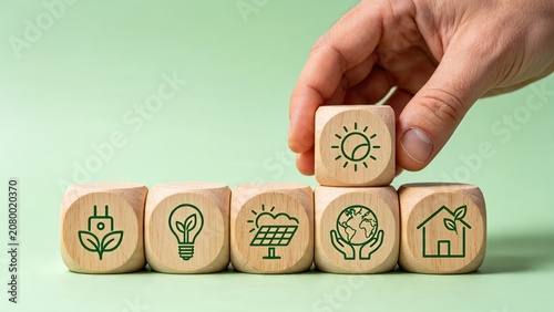 Hand placing wooden block with sun icon on top of eco symbols, representing sustainable energy, green environment, and ecological future concepts for business.