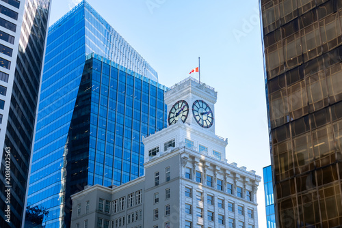 City view with skyscrapers built of concrete and glass, minimal and simple design and a building with a clock and a flag. Urban architecture in the business district. Vancouver, BC, Canada.