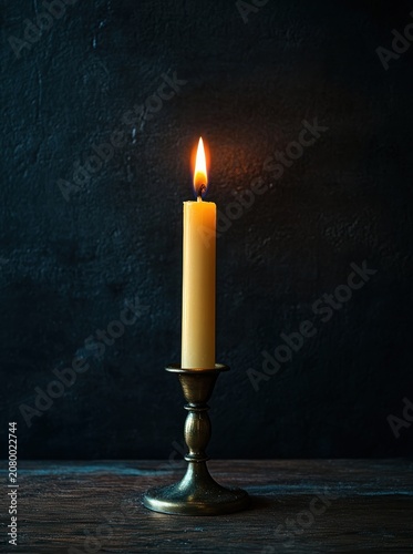 single lit taper candle in brass candlestick on wooden table against dark textured wall, warm glow evoking solitude and calm