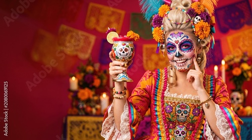 Woman with vibrant Day of the Dead sugar skull face paint, marigold floral headdress with feathers, holding decorated ceramic cup, wearing embroidered orange and pink dress.