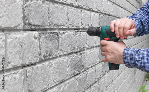 Close up of worker hand drilling into a gray brick wall with cordless electric screwdriver