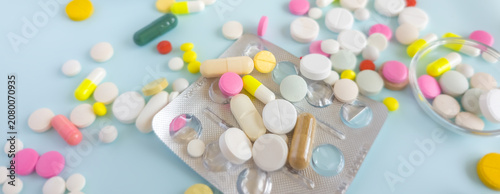Top view of colorful medical pills, capsules, and tablets spilled on bright yellow background