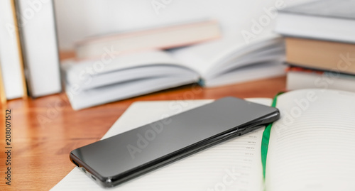Black smartphone screen down on a table with books in background