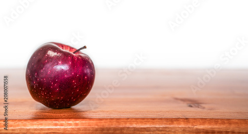 Vibrant Red Apple lying on the left side of a warm wooden surface with copy space