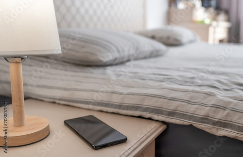Black smartphone lying on a wooden nightstand next to a bed