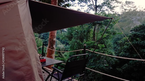 Cozy glamping tent with a shaded outdoor seating area overlooking a lush tropical forest, offering a peaceful nature retreat and scenic camping experience.