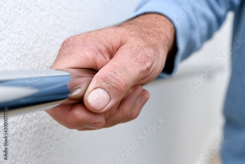 Elderly man's hand gripping a sturdy metal handrail for support and safety
