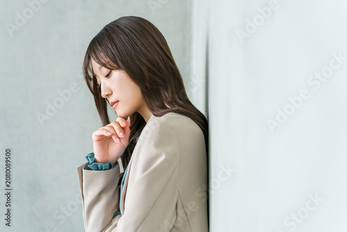 A young Asian businesswoman with her head bowed and arms crossed (thinking, worrying, feeling ennui, anxious).