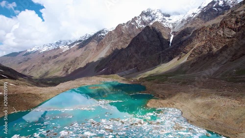 4K aerial landscape of turquoise blue Ghepan lake with small icebergs floating on its surface. Snow-capped peaks and High altitude glacial lake at Lahaul, Himachal Pradesh, India. Travel India concept