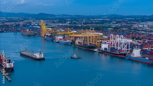 cargo ship guided by tugboats arrives at a massive commercial port terminal featuring gantry cranes and shipping containers, showcasing global maritime logistics and international trade.