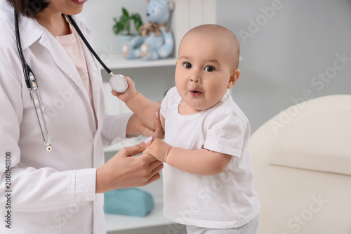 Young female pediatrician with happy little baby on couch in clinic, closeup