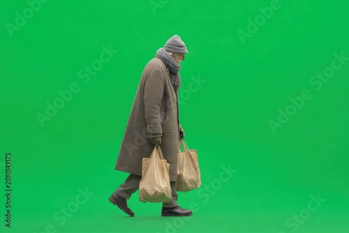 Elderly person walking, carrying bags, green background
