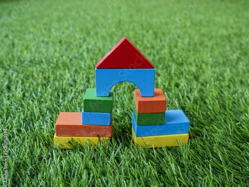 Vibrant multi-colored wooden shapes constructed into a small arch building over a fake grass mat.