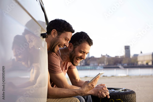 Two laughing men sitting in car looking at digital tablet