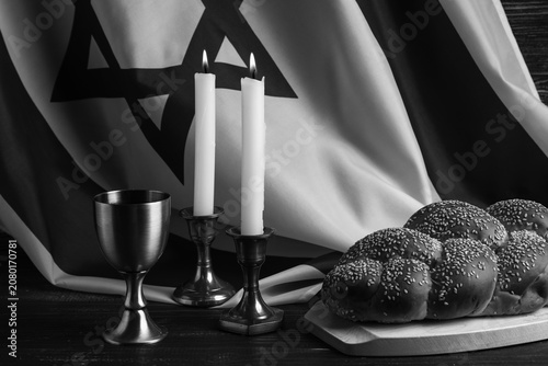 Photos Traditional challah bread with flag of Israel, wine goblet and burning candles on wooden table