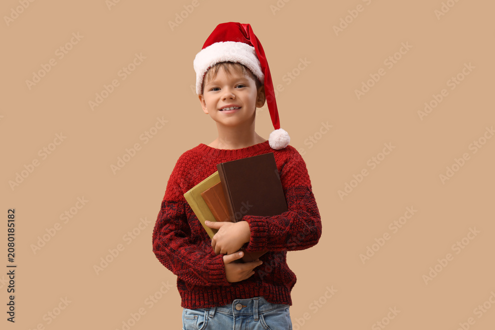 Obraz premium Cute little boy in Santa hat with books on beige background