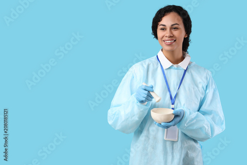 Happy young African-American female scientist with mortar and pestle on blue ...