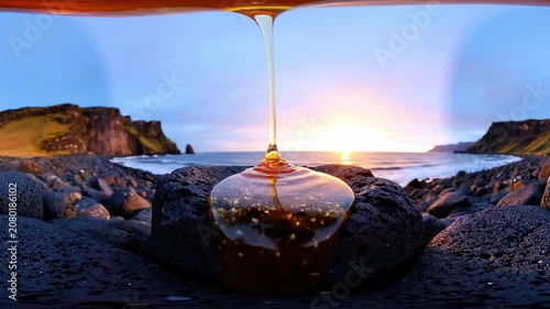 Golden liquid pours onto a dark rock by the ocean at sunset