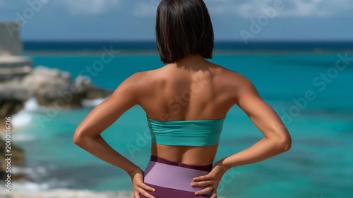 Fit woman standing by turquoise sea wearing wireless earbuds
