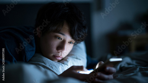 暗闇の中スマホの画面だけが照らす男性の横顔 ｜ 青いネオン光