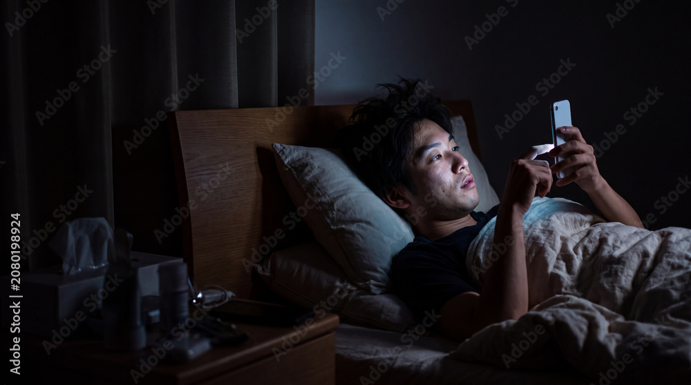 Fototapeta premium 真剣な表情でメッセージを確認する夜のベッドの男性 ｜ 緊張感ある視線