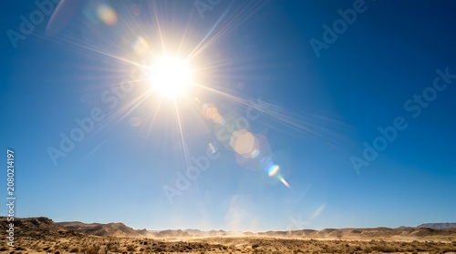 Bright sun high in clear blue sky over rocky desert symbolizing harsh summer heat and drought
