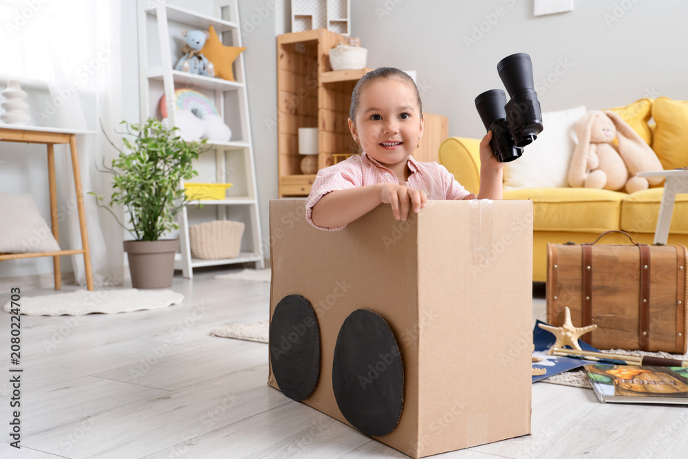 Obraz premium Cute little girl with binoculars in cardboard car at home