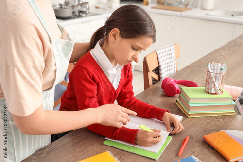 Cute schoolgirl doing homework with her mother in kitchen