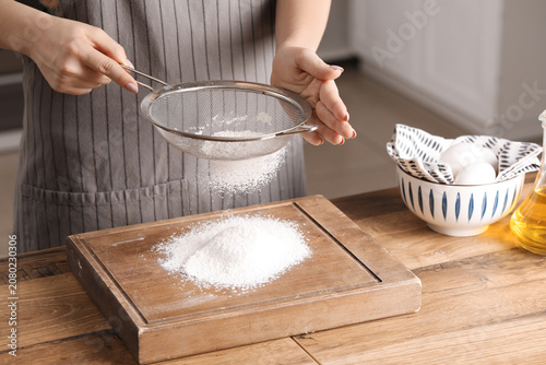 Bilde på lerret Woman with sieve sifting flour on table in kitchen
