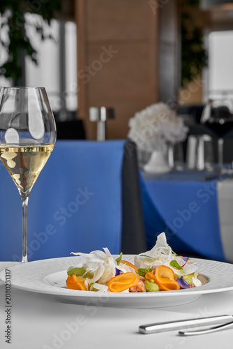 Canvastavla Gourmet seafood appetizer with shaved fennel and a glass of white wine in a luxury restaurant interior with blue accents