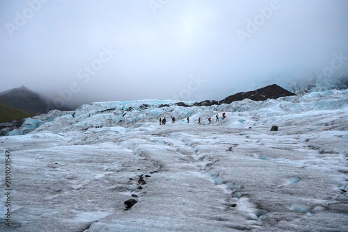 Bild auf Leinwand Group of hikers walking on the surface of the Vatnajökull glacier, amidst blue ice formations and fog, Iceland