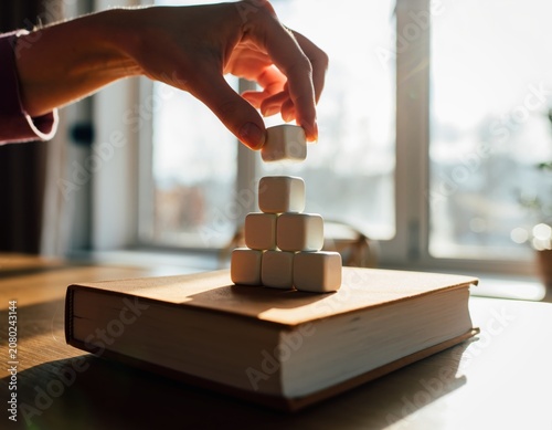 Hand placing a white cube on a pyramid stack on a book