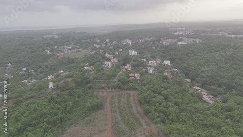 Aerial view of houses in Old Goa surrounded by lush greenery during the pre-monsoon season, with a dramatic sunset glowing through cloudy skies over the scenic landscape.