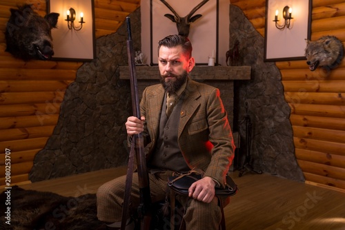 Hunter in traditional tweed clothing sitting and holding his rifle vertically