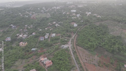 Aerial view of houses in Old Goa surrounded by lush greenery during the pre-monsoon season, with a dramatic sunset glowing through cloudy skies over the scenic landscape.