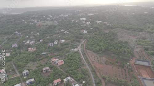 Aerial view of houses in Old Goa surrounded by lush greenery during the pre-monsoon season, with a dramatic sunset glowing through cloudy skies over the scenic landscape.