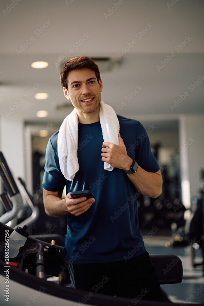 Obraz premium Happy athletic man using app on cell phone during sports training in health club.