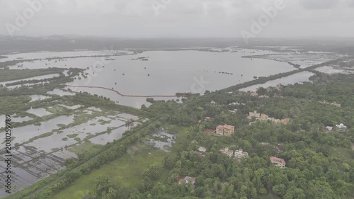 Aerial view of Old Goa and the Mandovi River during the monsoon season, featuring coconut palms, green fields, backwaters, lush greenery, nearby houses, and cloudy skies.