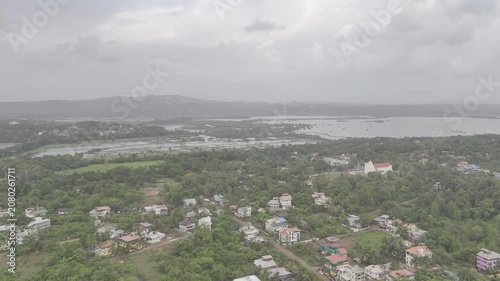 Aerial view of Old Goa and nearby houses along the Mandovi River during the monsoon season, featuring cloudy skies, lush surroundings, and the scenic riverside landscape of Goa.