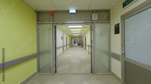 Modern clinic hallway features electrical switchboards safety handrails and exit signs. Bright ceiling lights create pristine atmosphere